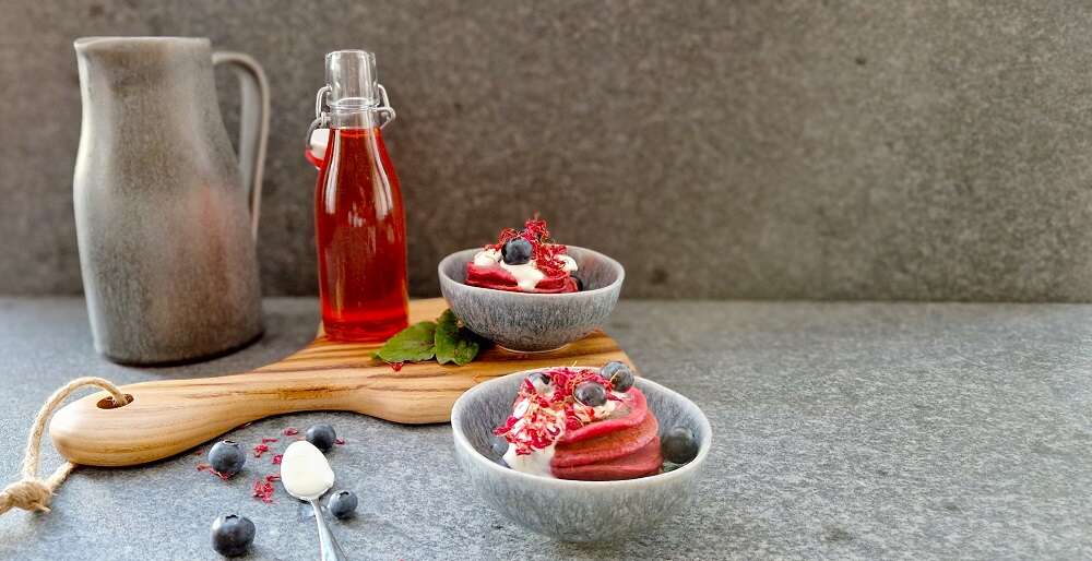 Schüsseln mit Pancakes, Sirup, Beeren und Rahm