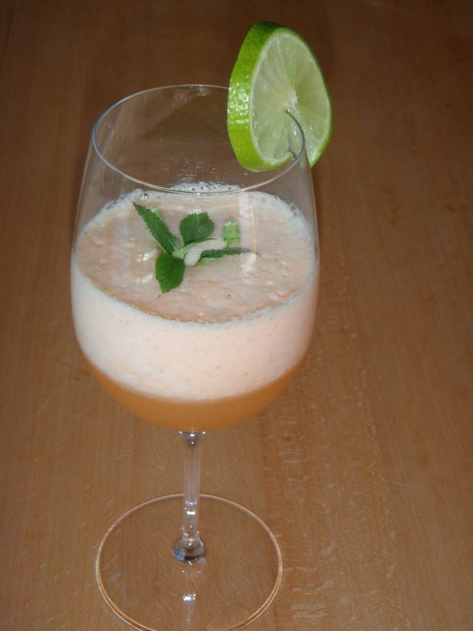 Weinglas mit Cocktail, Süsskrautblättern und Limettenscheibe