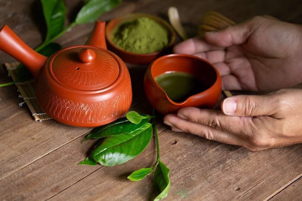 Tè verde in vaso rosso e foglie di tè verde